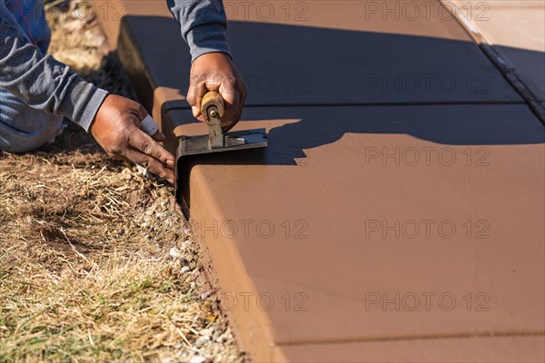 Construction worker smoothing wet cement with curb tool