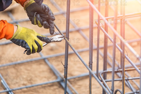 Worker securing steel rebar framing with wire plier cutter tool at construction site