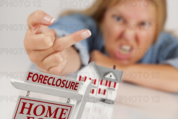 Angry woman flipping the bird behind model home and foreclosure real estate sign in front
