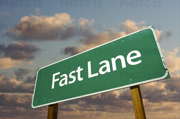Fast lane green road sign over dramatic clouds and sky