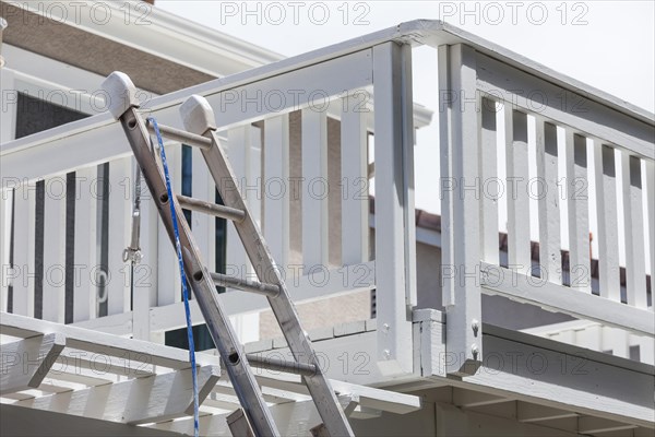 Construction ladder and painting hose leaning on white house deck