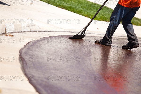 Road worker resurfacing street with hot tar