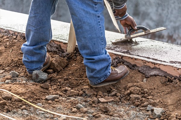 Construction worker using wood trowel on wet cement forming coping around new pool