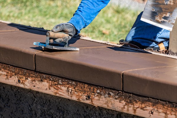 Construction worker using hand groover on wet cement forming coping around new pool