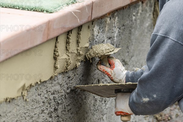 Tile worker applying cement with trowel at pool construction site