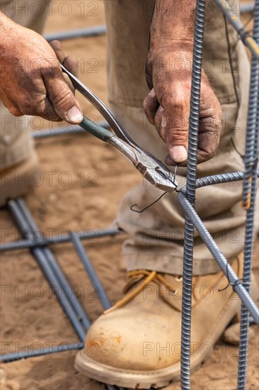 Worker securing steel rebar framing with wire plier cutter tool at construction site