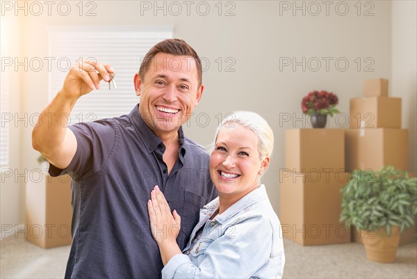 Happy couple with new house keys inside empty room with boxes
