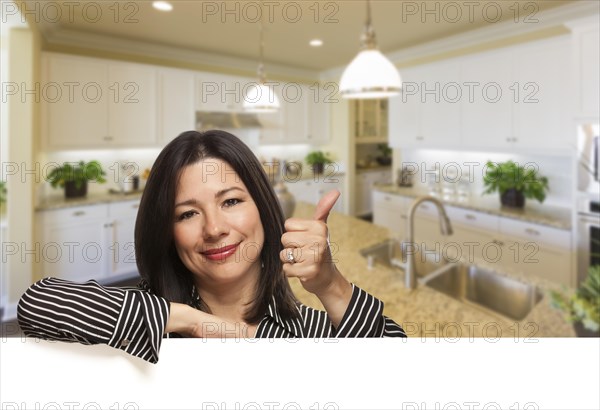 Smiling hispanic woman with thumbs up in beautiful custom kitchen