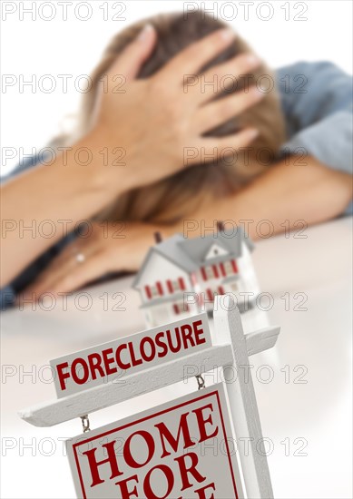 Woman with head in hand behind model home and foreclosure real estate sign in front