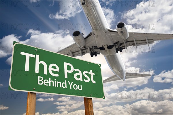 The past green road sign and airplane above with dramatic blue sky and clouds