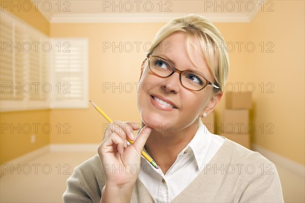 Attractive daydreaming woman holding pencil in empty room and boxes