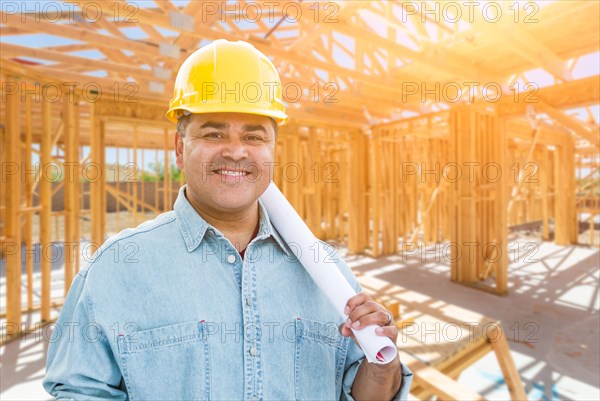 Hispanic male contractor with blueprint plans wearing hard hat at construction site