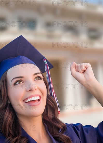 Happy graduating mixed-race woman in cap and gown celebrating on campus