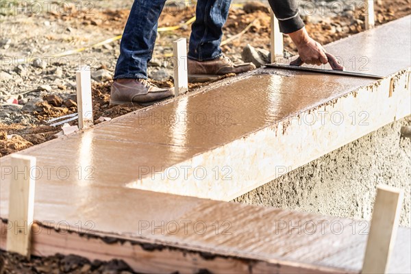 Construction worker using wood trowel on wet cement forming coping around new pool