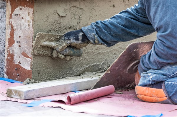 Tile worker applying cement with trowel at pool construction site