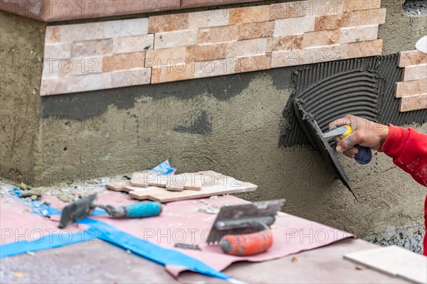 Worker installing wall tile cement with trowel and tile at construction site