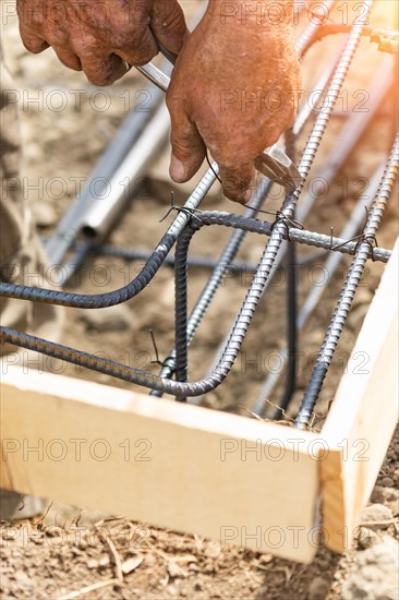 Worker securing steel rebar framing with wire plier cutter tool at construction site