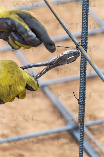 Worker securing steel rebar framing with wire plier cutter tool at construction site