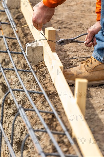 Worker securing steel rebar framing with wire plier cutter tool at construction site