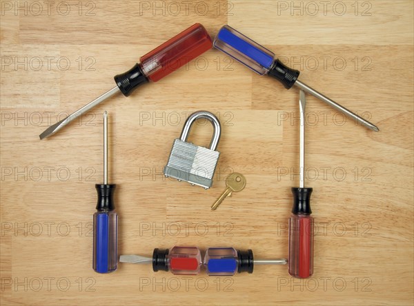 House shaped by screwdrivers with lock and key on a wood background