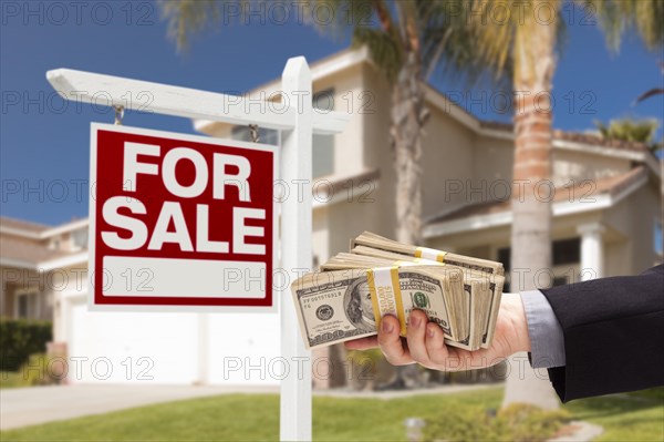 Buyer handing over cash for house with home and for sale real estate sign behind