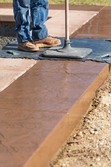 Construction worker applying pressure to texture template on wet cement