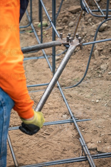 Worker using tools to bend steel rebar at construction site