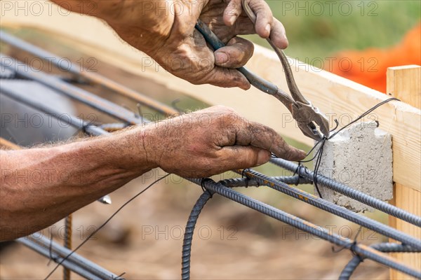 Worker securing steel rebar framing with wire plier cutter tool at construction site