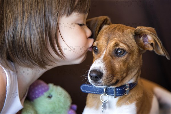 Toddler girl kissing her puppy dog