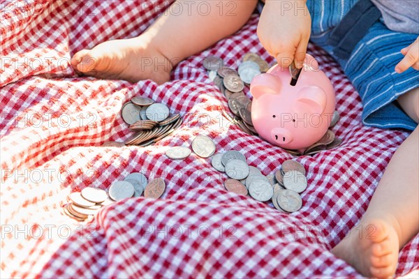 Baby boy sitting on picnic blanket putting coins in piggy bank