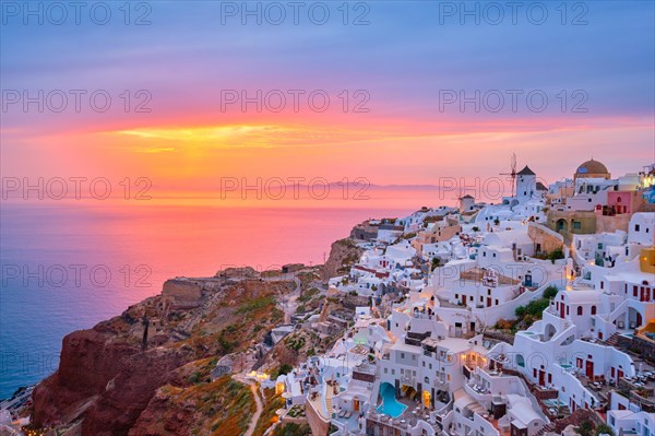 Famous greek iconic selfie spot tourist destination Oia village with traditional white houses and windmills in Santorini island on sunset in twilight