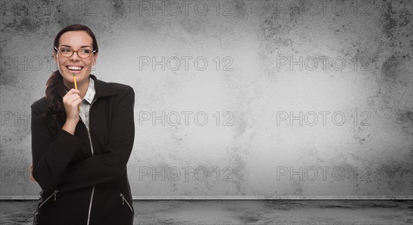 Young adult woman with pencil and glasses standing in front of blank grungy blank wall with copy space