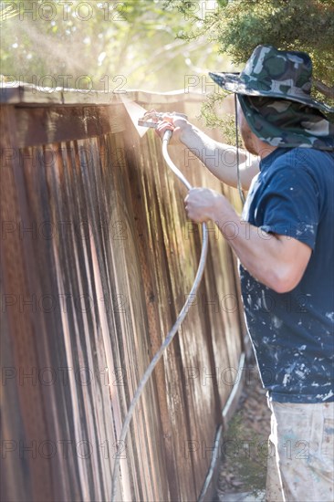 Professional painter spraying house yard fence with wood stain