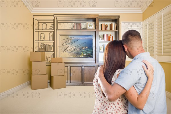 Young military couple looking at drawing of entertainment unit in room with moving boxes
