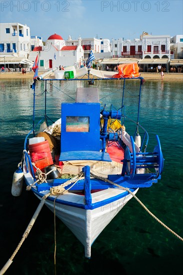 Blue fishing boat in port harbor of Chora town on Mykonos island with orthodox church in background