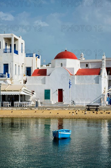 Blue fishing boat in port harbor of Chora town on Mykonos island with orthodox church in background