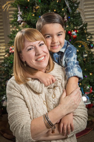 Happy mother and mixed-race son hug near their christmas tree