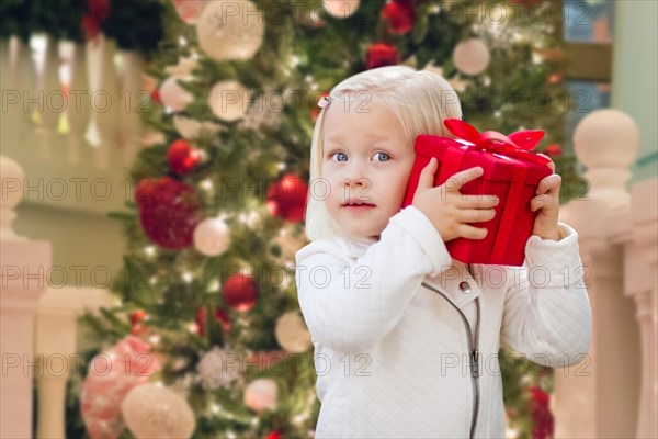 Happy young girl holding gift box in front of decorated christmas tree