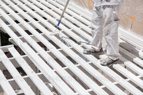 Professional painter rolling white paint onto the top of A home patio cover