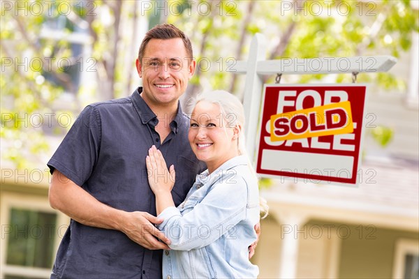 Caucasian couple in front of sold real estate sign and house