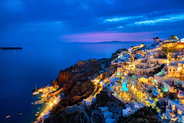 Famous greek iconic selfie spot tourist destination Oia village with traditional white houses and windmills in Santorini island in the evening blue hour