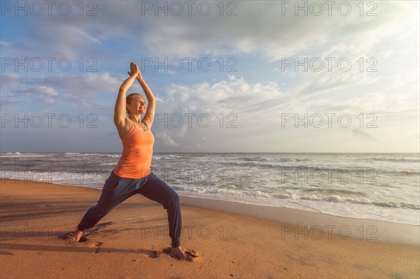Woman doing Hatha yoga asana Virabhadrasana 1 Warrior Pose outdoors on ocean beach on sunset. Kerala