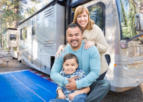 Happy young mixed-race family in front of their beautiful RV at the campground