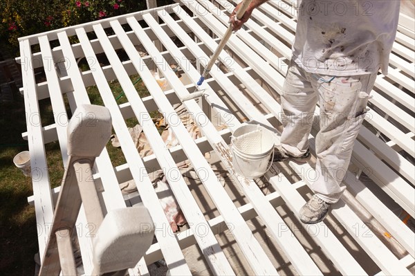 Professional painter rolling white paint onto the top of A home patio cover