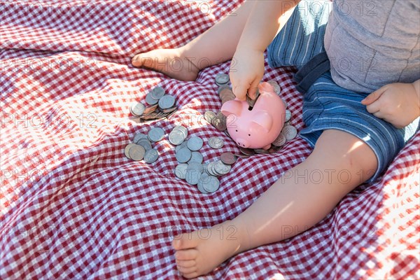 Baby boy sitting on picnic blanket putting coins in piggy bank