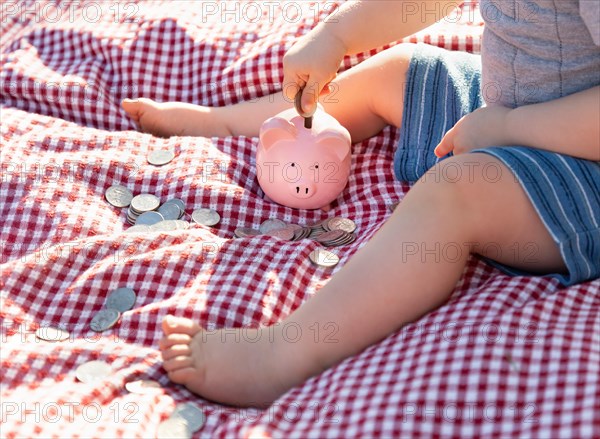 Baby boy sitting on picnic blanket putting coins in piggy bank