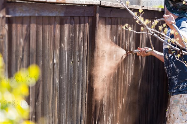 Professional painter spraying house yard fence with wood stain