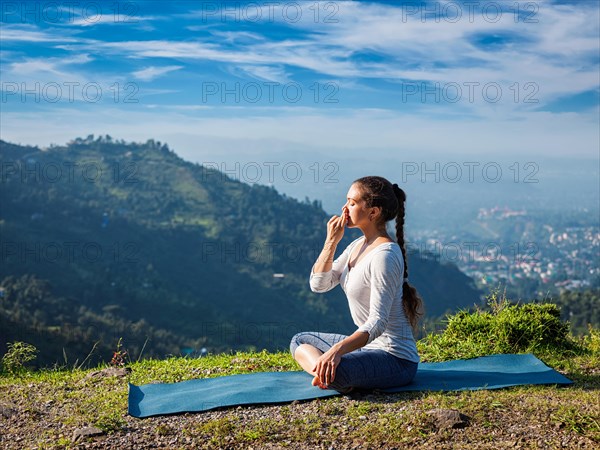 Woman practices pranayama yoga breath control in lotus pose padmasana outdoors in Himalayas in the morning on sunrise. Himachal Pradesh