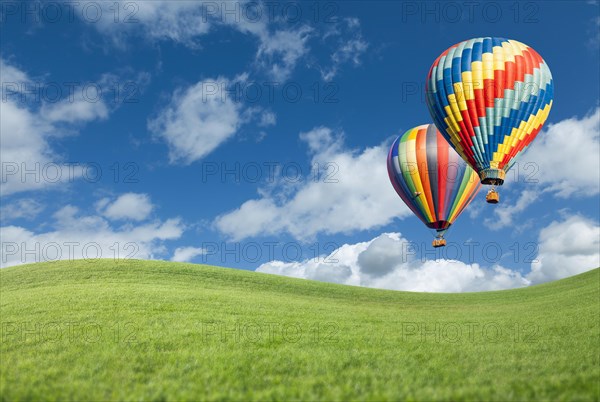 Two hot air balloons up in the beautiful blue sky with grass field below