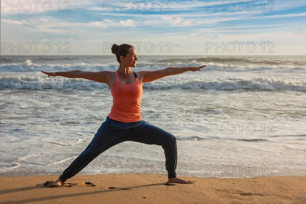 Woman doing Hatha yoga asana Virabhadrasana 1 Warrior Pose outdoors on ocean beach on sunset. Kerala